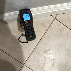 Moisture meter reading on a wet tile floor next to a water stain