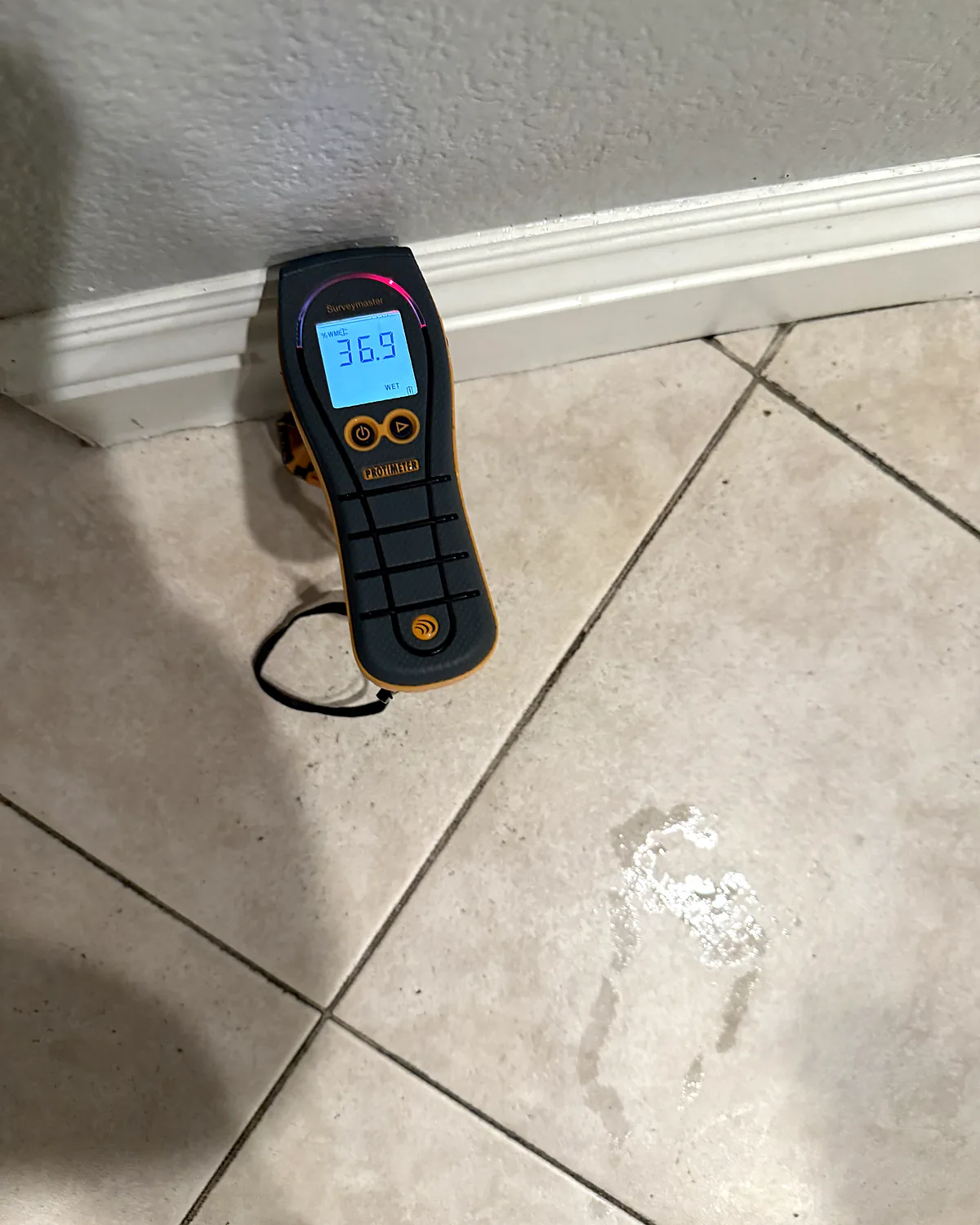Moisture meter reading on a wet tile floor next to a water stain